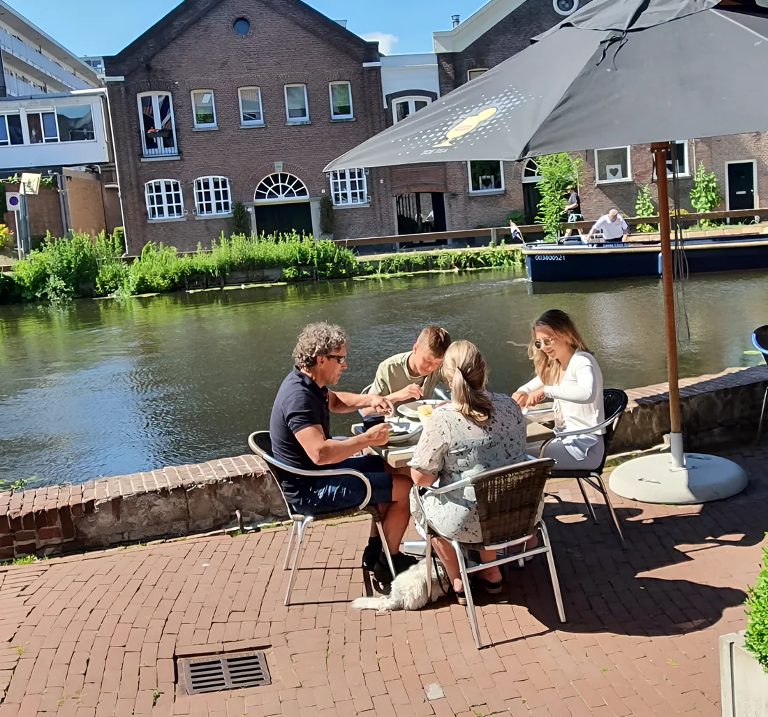 Het terras aan de Noordvest op een zomerse dag: gasten aan tafel langs de kade, met een boot op de gracht