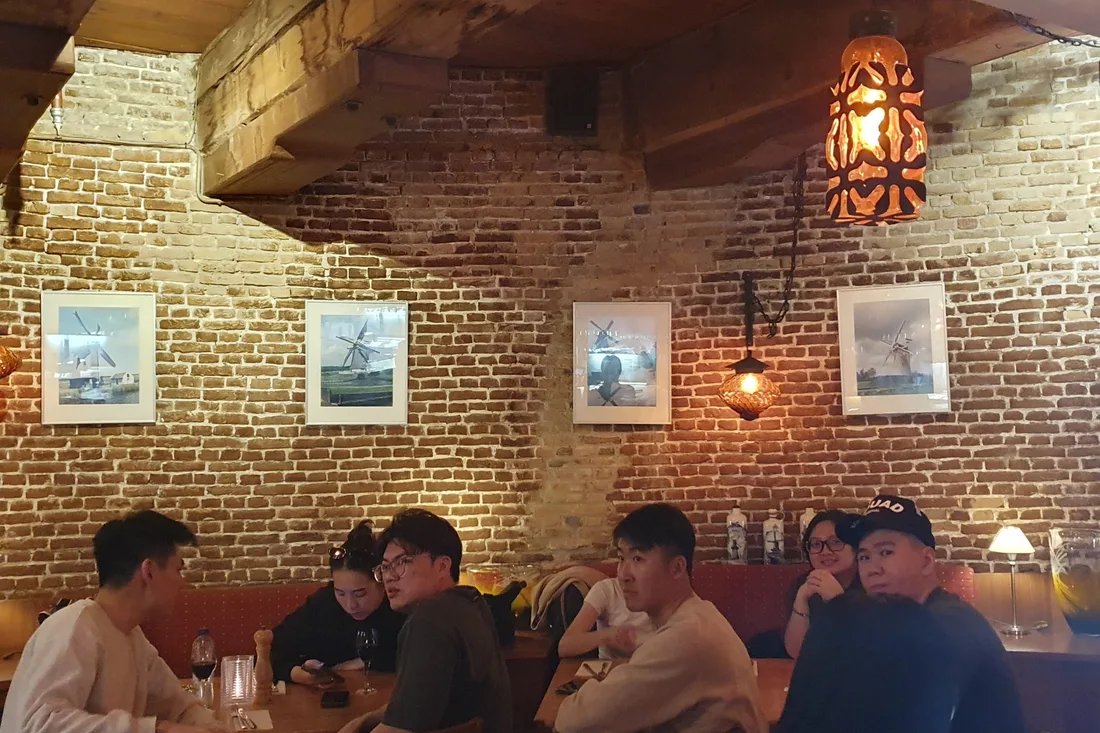 Een gezelschap aan de lange tafels in de molen, onder de balken en de molenprenten aan de bakstenen muur